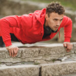 Man in a red hoodie doing push-ups on outdoor stone steps