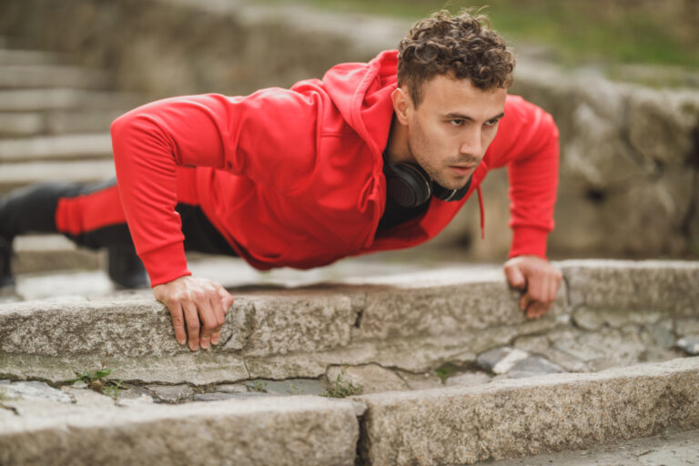 Man in a red hoodie doing push-ups on outdoor stone steps