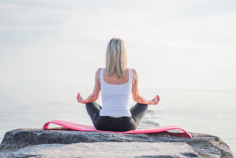 Woman meditating cross-legged on a rock by the sea