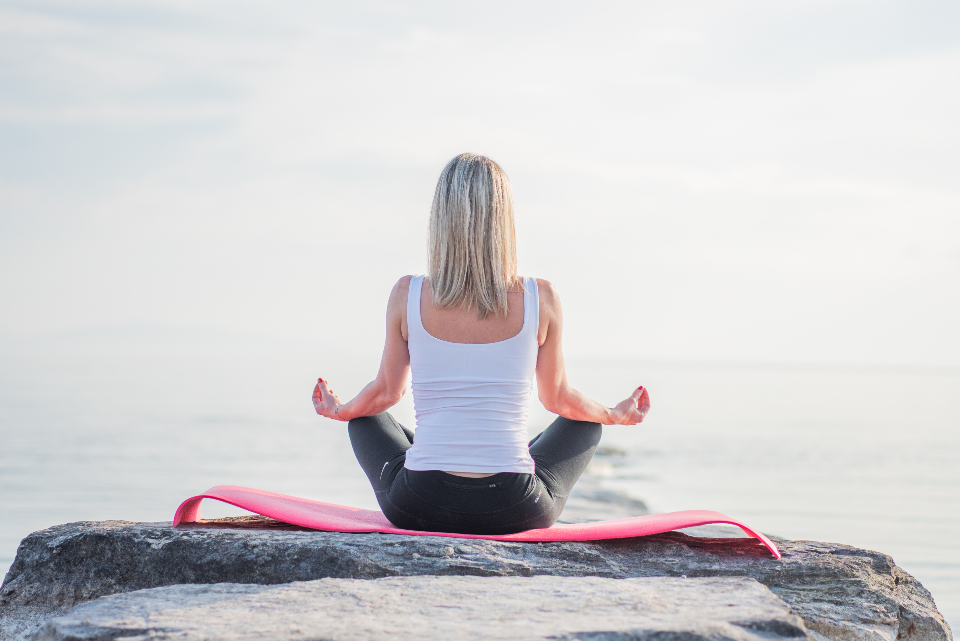 Woman meditating cross-legged on a rock by the sea