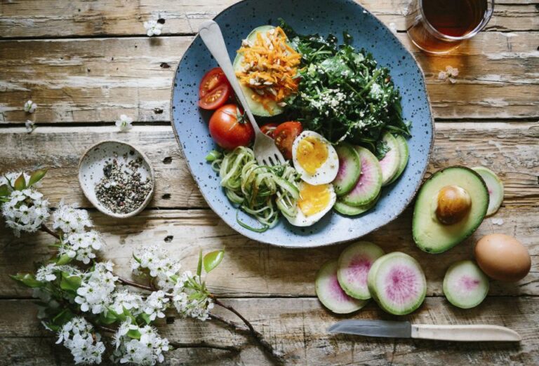 Balanced plate with greens, eggs, tomatoes and avocado on a rustic table