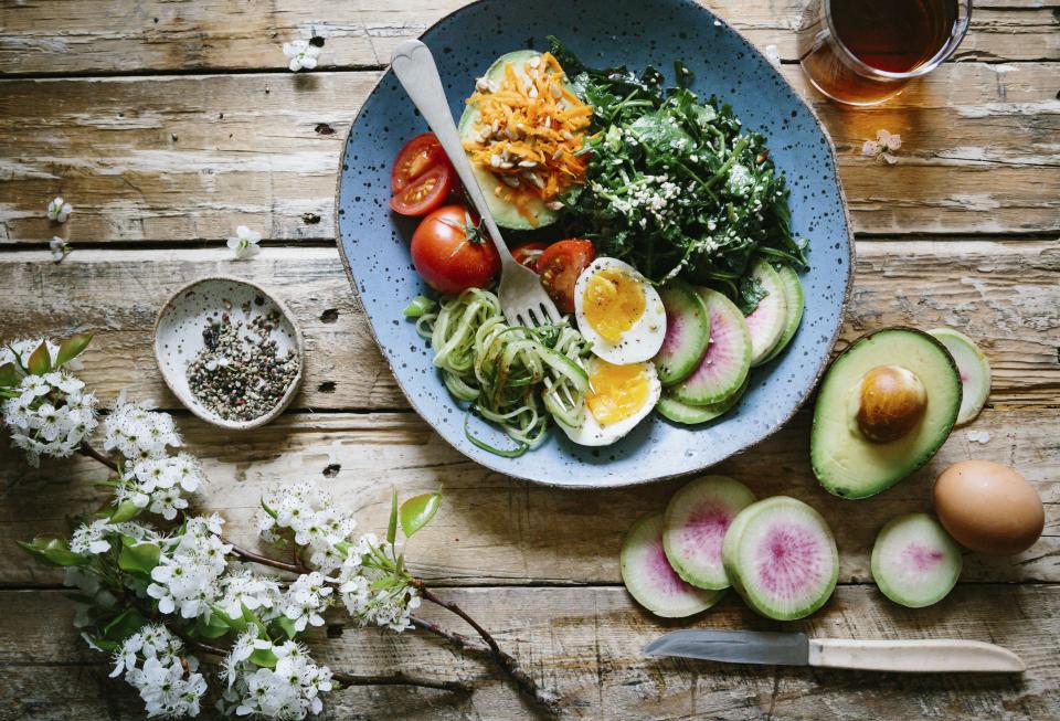 Balanced plate with greens, eggs, tomatoes and avocado on a rustic table