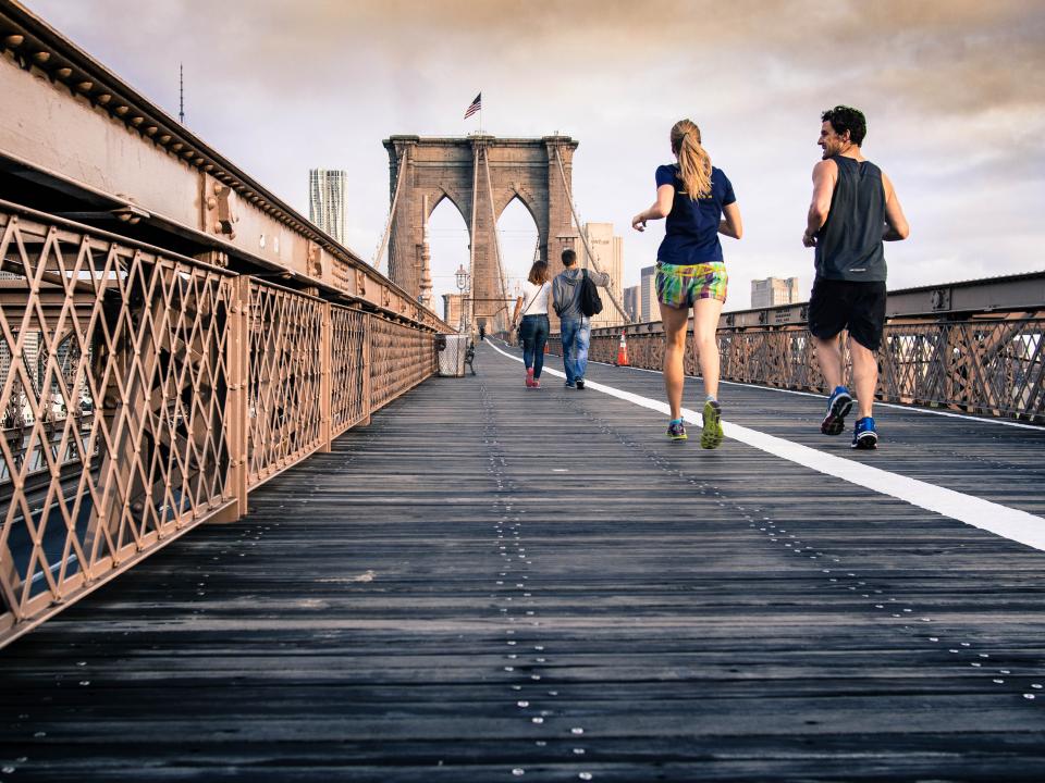 Two runners jogging across a wooden bridge walkway toward the city