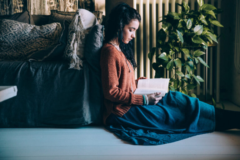 Woman reading a book on a cozy window seat beside a plant