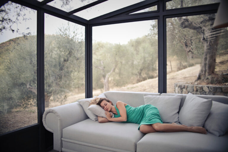 Woman napping peacefully on a sofa in a bright sunroom