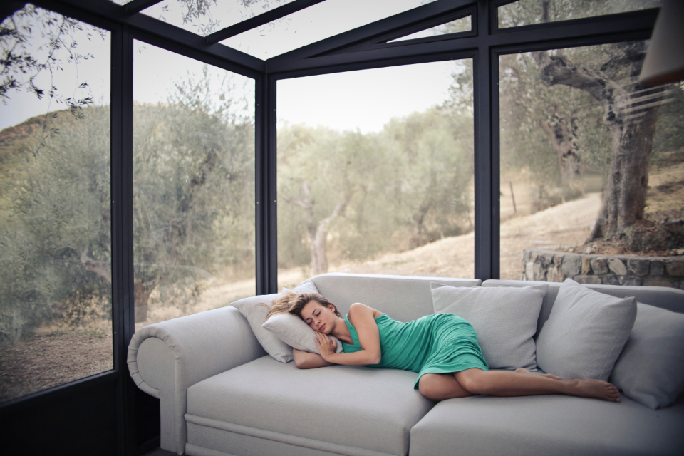 Woman napping peacefully on a sofa in a bright sunroom