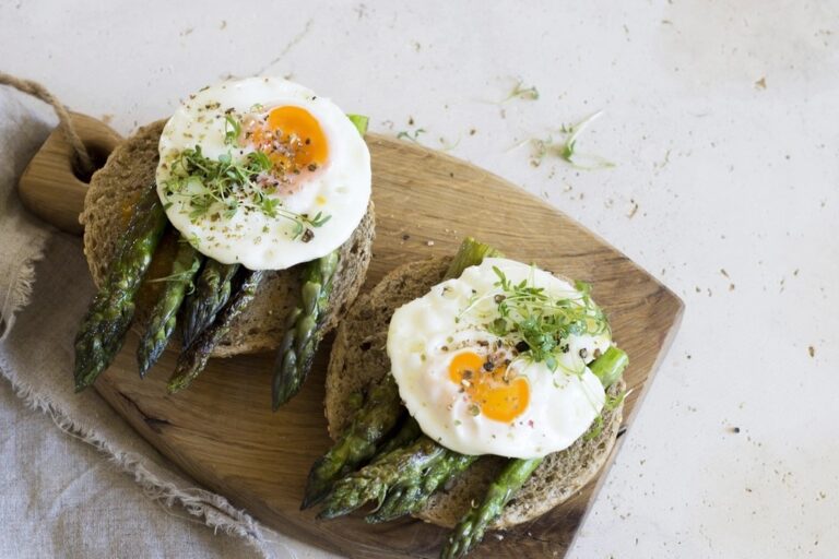 Fried eggs with asparagus on wholegrain toast on a wooden board