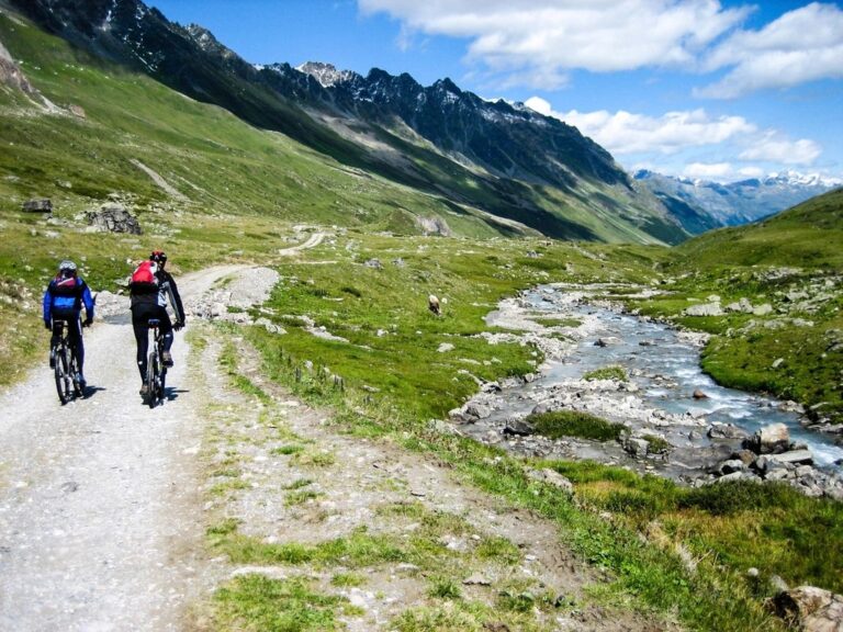 Two cyclists riding a gravel path through a green mountain valley