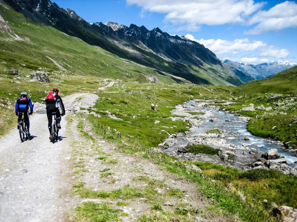 Two cyclists riding a gravel path through a green mountain valley