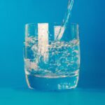 Water being poured into a clear glass against a blue background