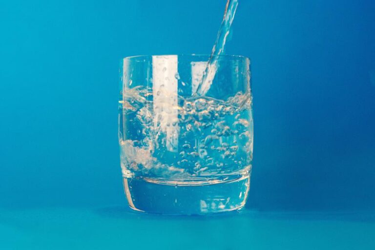 Water being poured into a clear glass against a blue background
