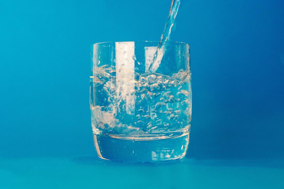 Water being poured into a clear glass against a blue background