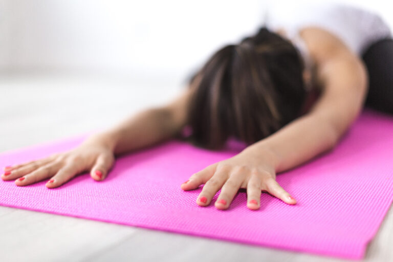 Woman resting in child's pose on a pink yoga mat