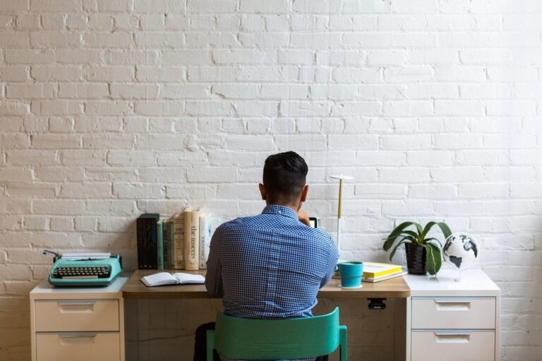 Man working at a tidy desk against a white brick wall