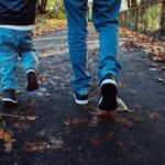 Two people walking along a park path covered in autumn leaves