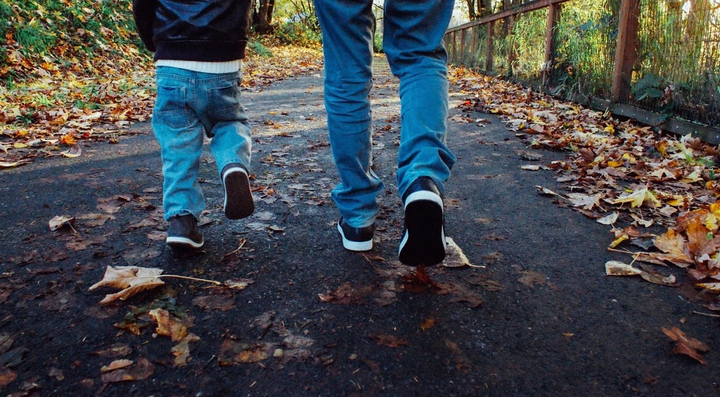 Two people walking along a park path covered in autumn leaves
